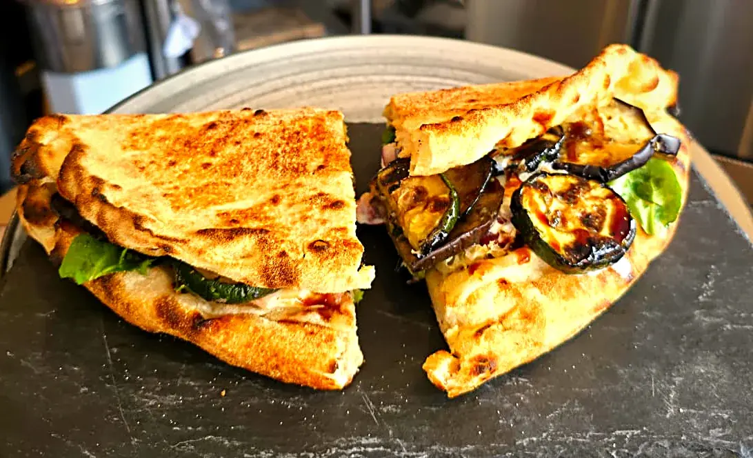 Le panozzo Bibi de Mémé Rina à Chatou, coupé en deux sur son ardoise : pâte dorée, aubergines et courgettes grillées, stracciatella, roquette et crème balsamique